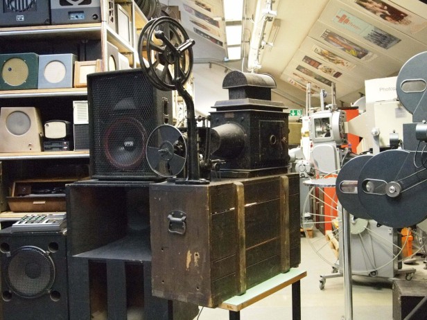 Für den Betrieb der Kohlenbogen-Lampe war Gleichstrom notwendig. Dieser wurde damals noch mit Gleichrichter-Röhren umgewandelt, die bei Betrieb ebenfalls leuchteten. Die beiden gläsernen Röhrendioden sind in der Holzkiste untergebracht.